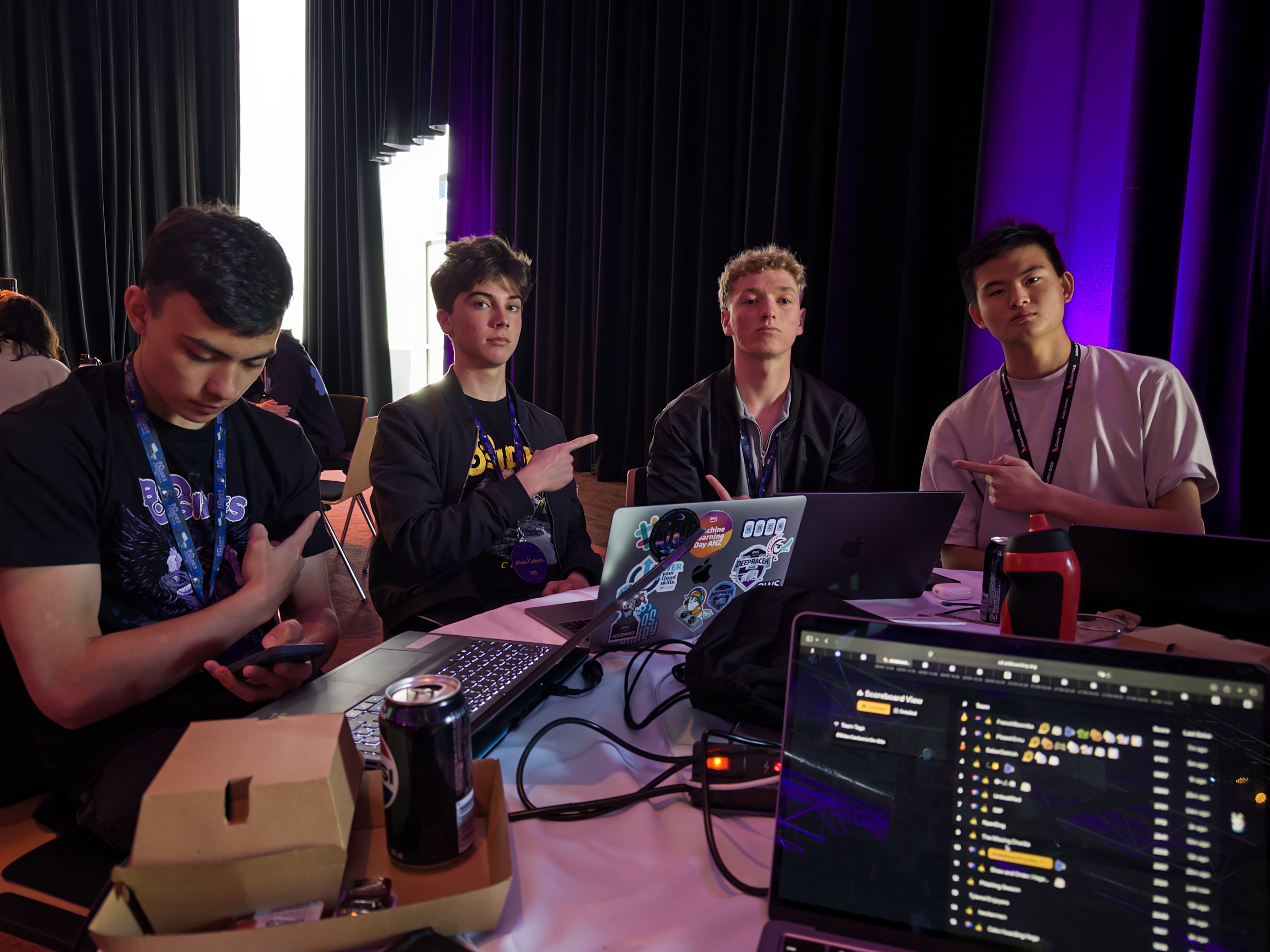 Jun and friends at a hackathon, laptops and code on screen, purple lights