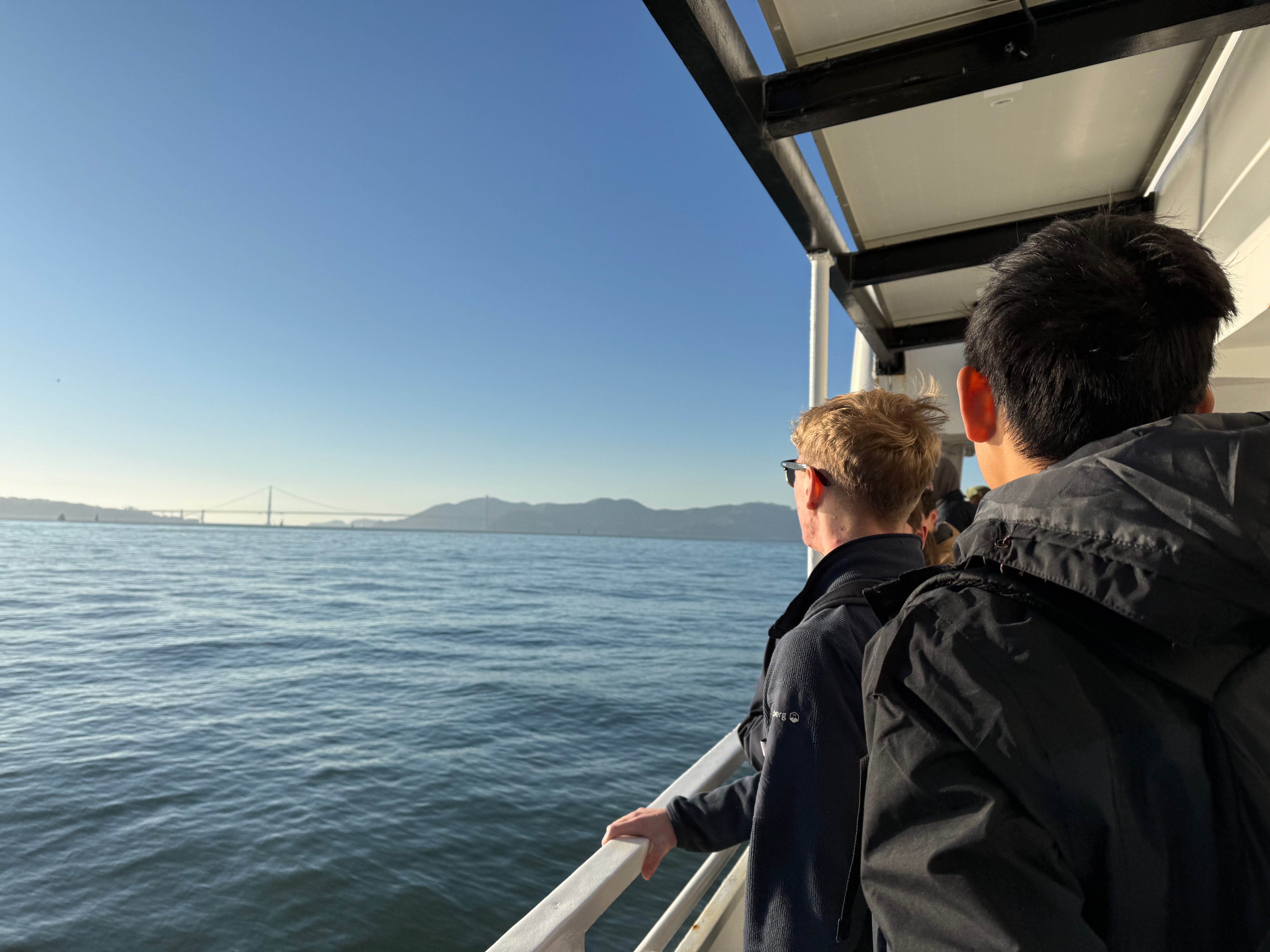 Two guys looking out from the ferry, bay and bridge in the distance