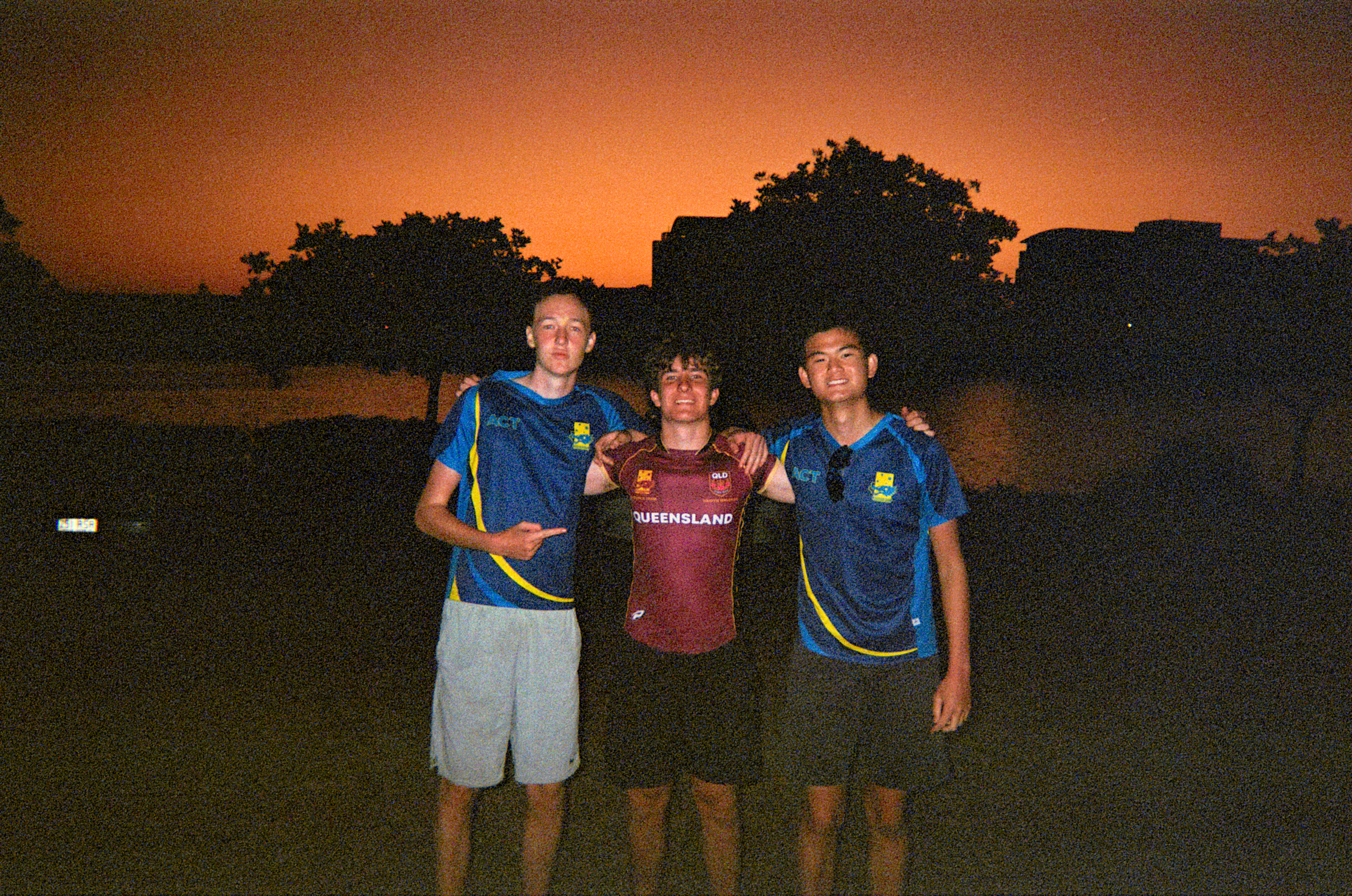 Three guys in team kit, warm orange sunset sky behind them on film