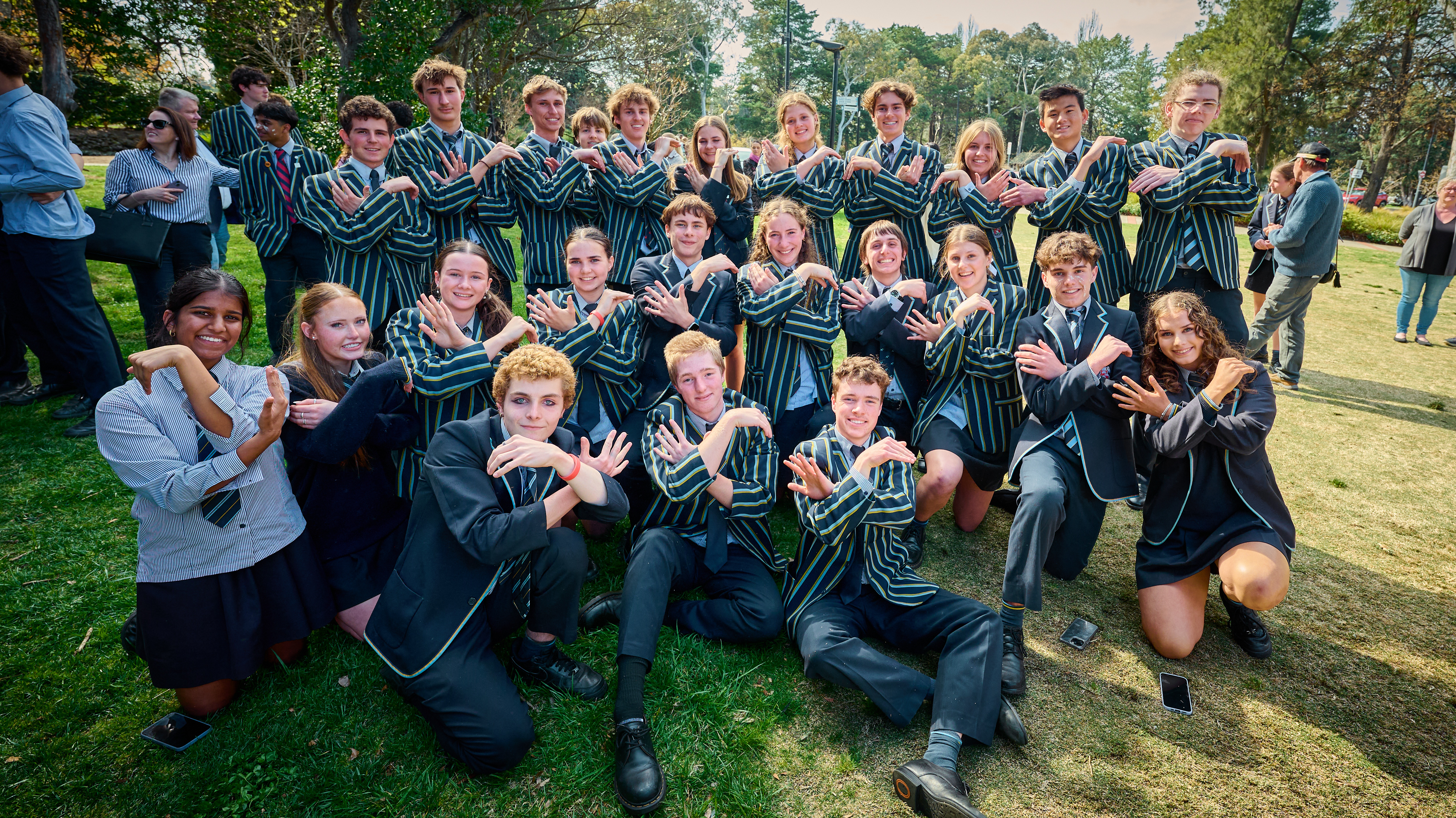The whole grade in school blazers on the lawn, doing the CGS hand sign